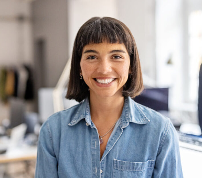 Portrait of confident hispanic woman standing in office. Happy female entrepreneur with short hair at office looking at camera.